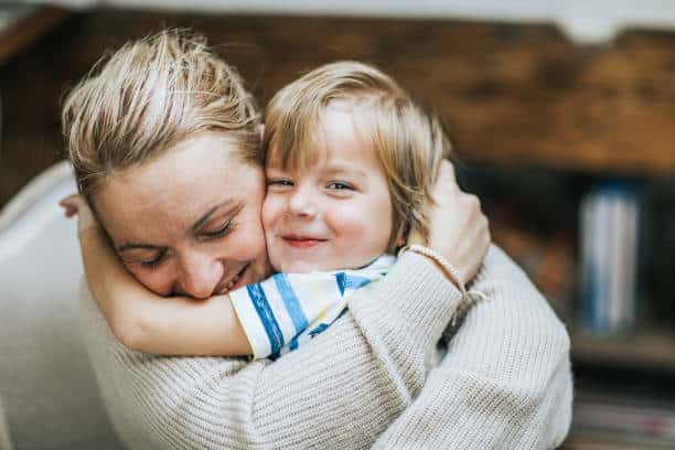 Happy mother embracing her small son at home while boy is looking at camera