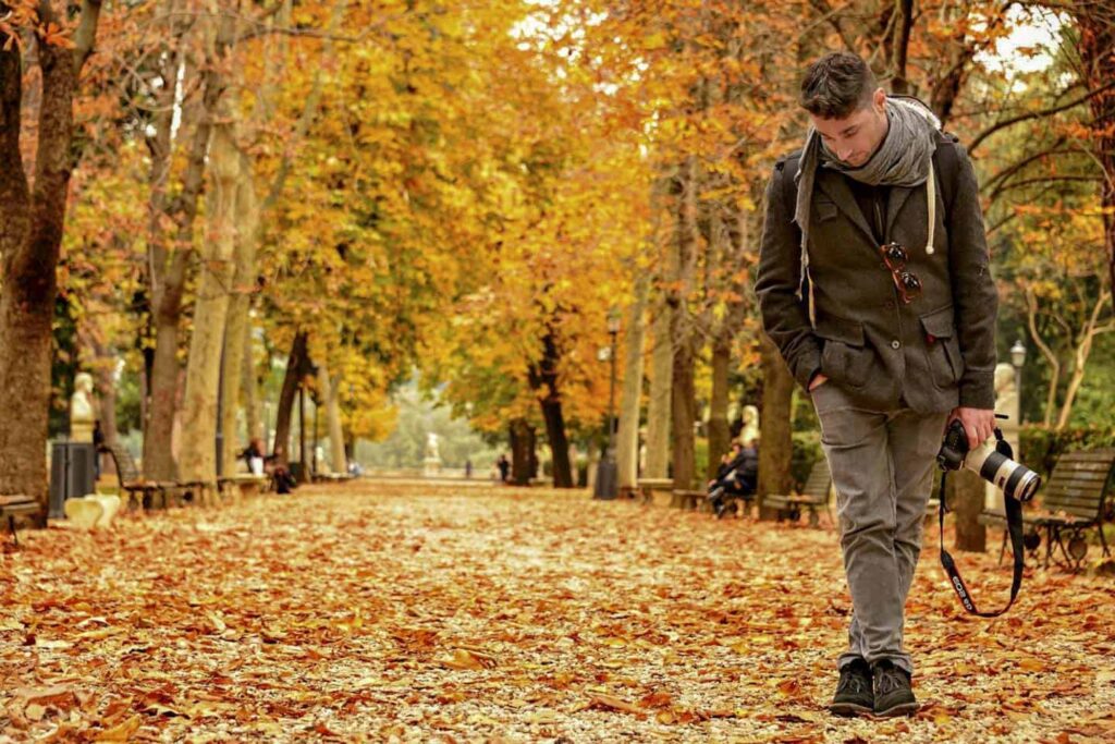 A view of a person looking down standing in autumn leaves in a forest with a camera in hand