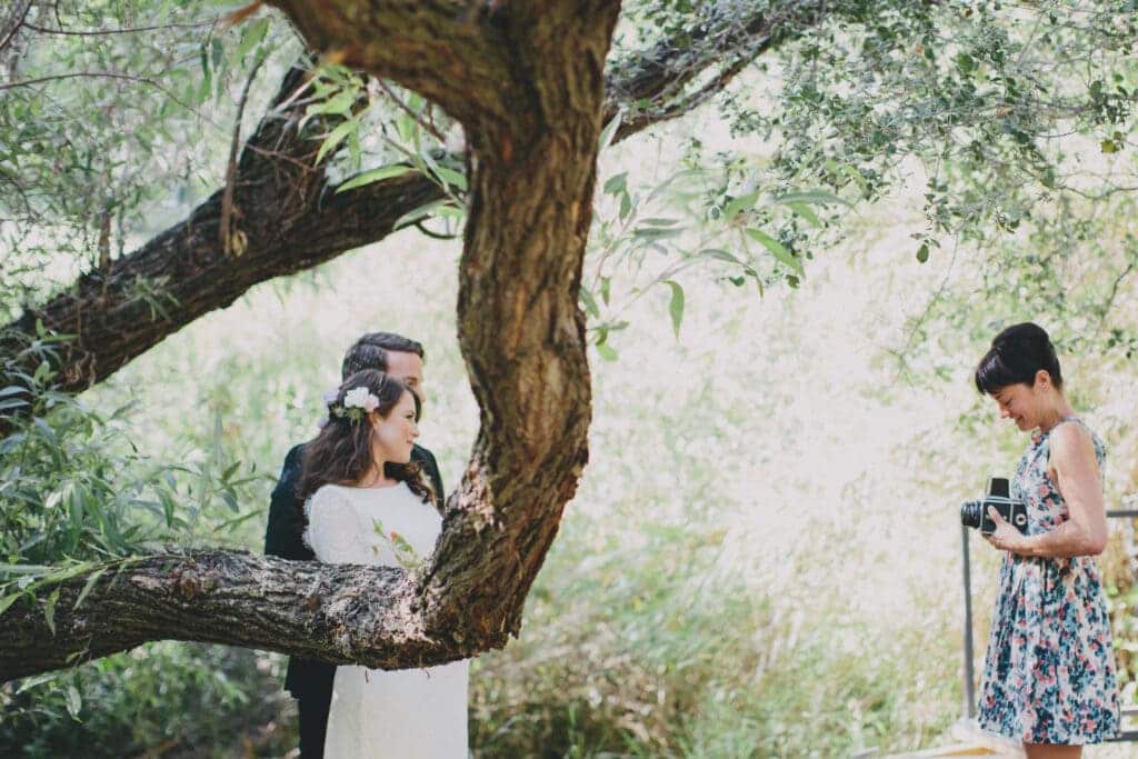 a female photographer capturing bride and groom near trees