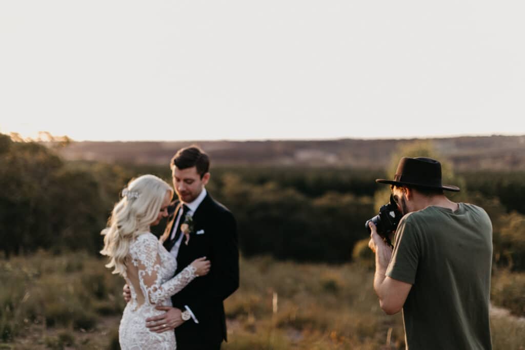 a phtographer in green shirt taking pictures of a groom and bride in a beautiful landscape