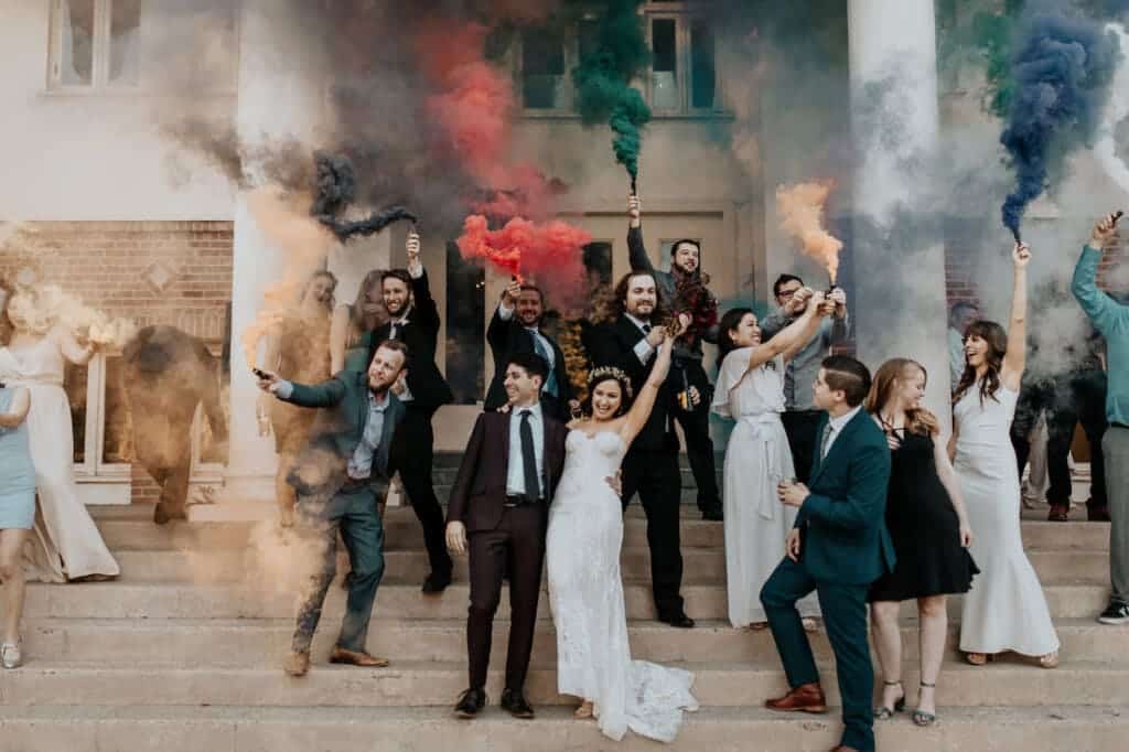 candid picture of bride groom and guests holding color bombs in different colors on a stair