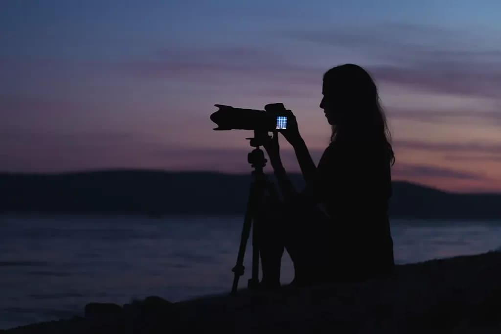 A dim view of girl adjusting the camera on a tripod