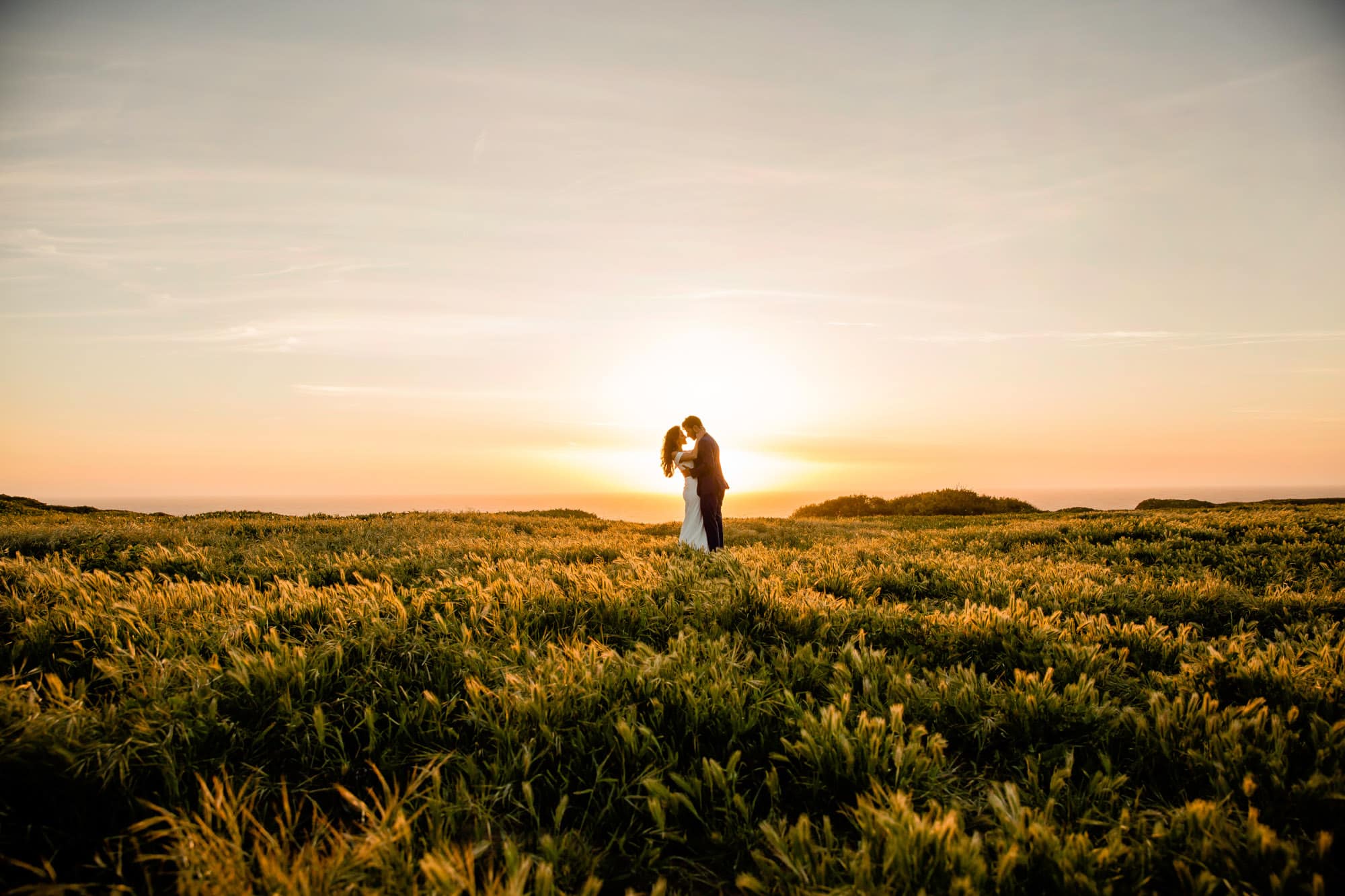 a couple standing in a green field during golden hour