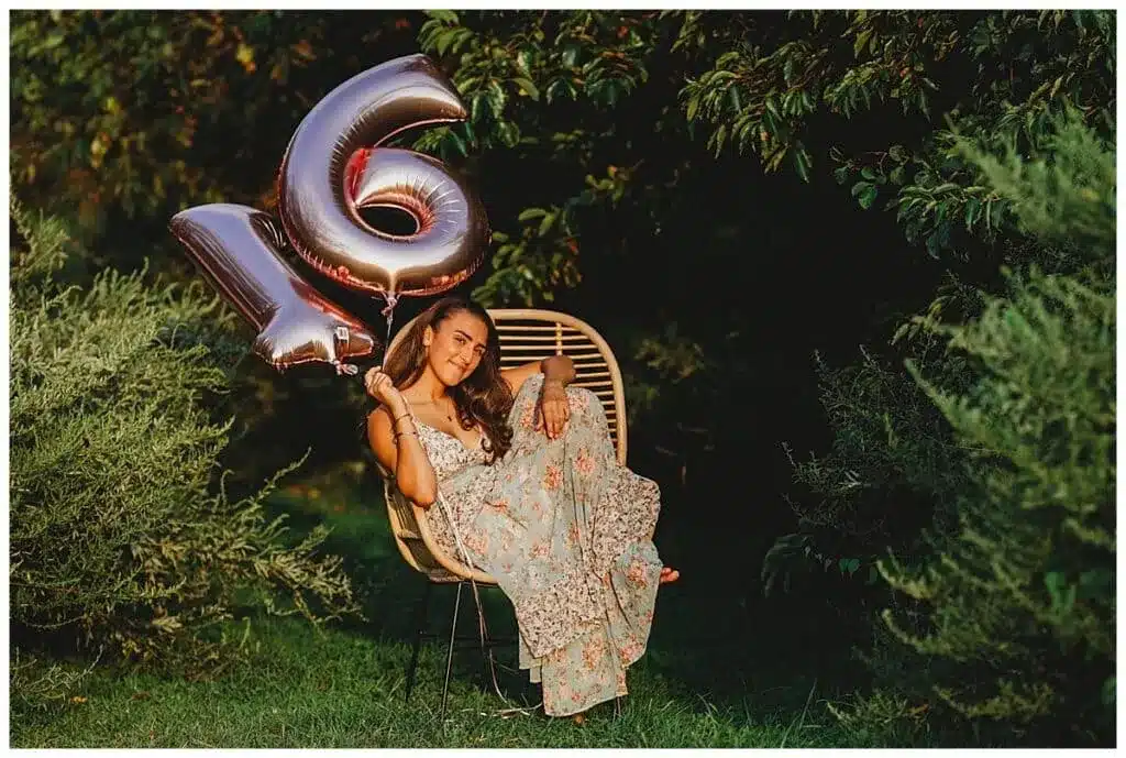 a girl sitting on a chair in the outdoor greenery holding th foil balloon