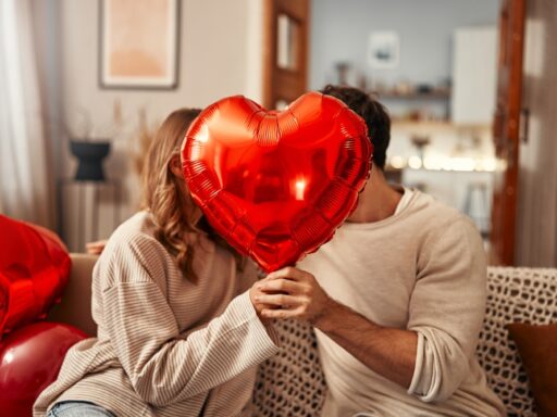 Young couple in love holding a heart-shaped balloon, covering themselves with it