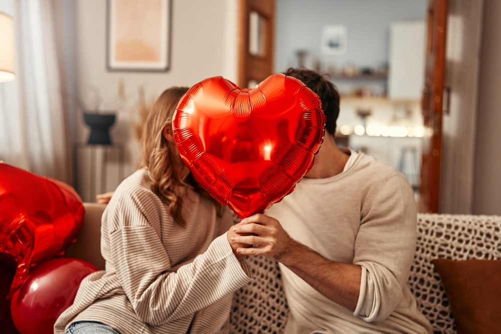 Young couple in love holding a heart-shaped balloon, covering themselves with it