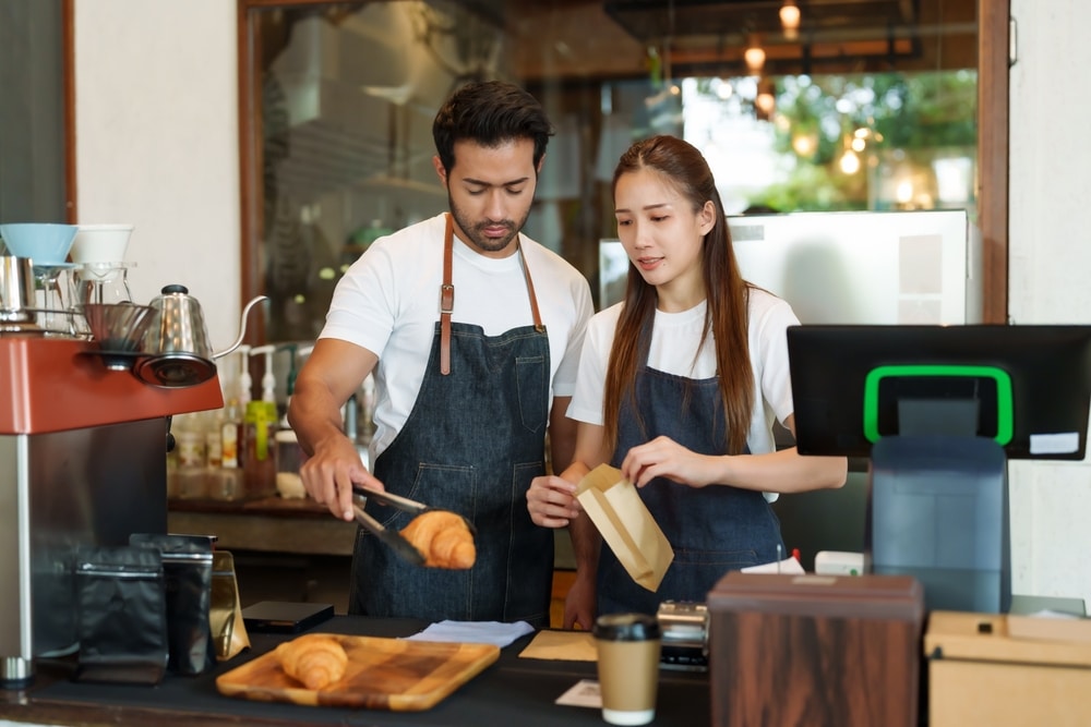 a couple baking Croissants in kitchen, wearing aprons