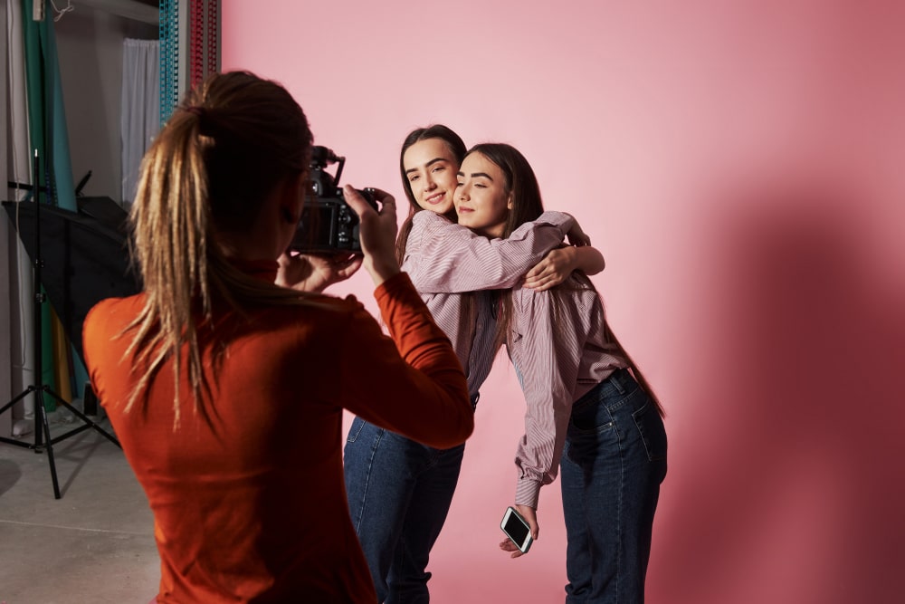 Picture of two girls that hug each and and are photographed by female cameraman in the studio
