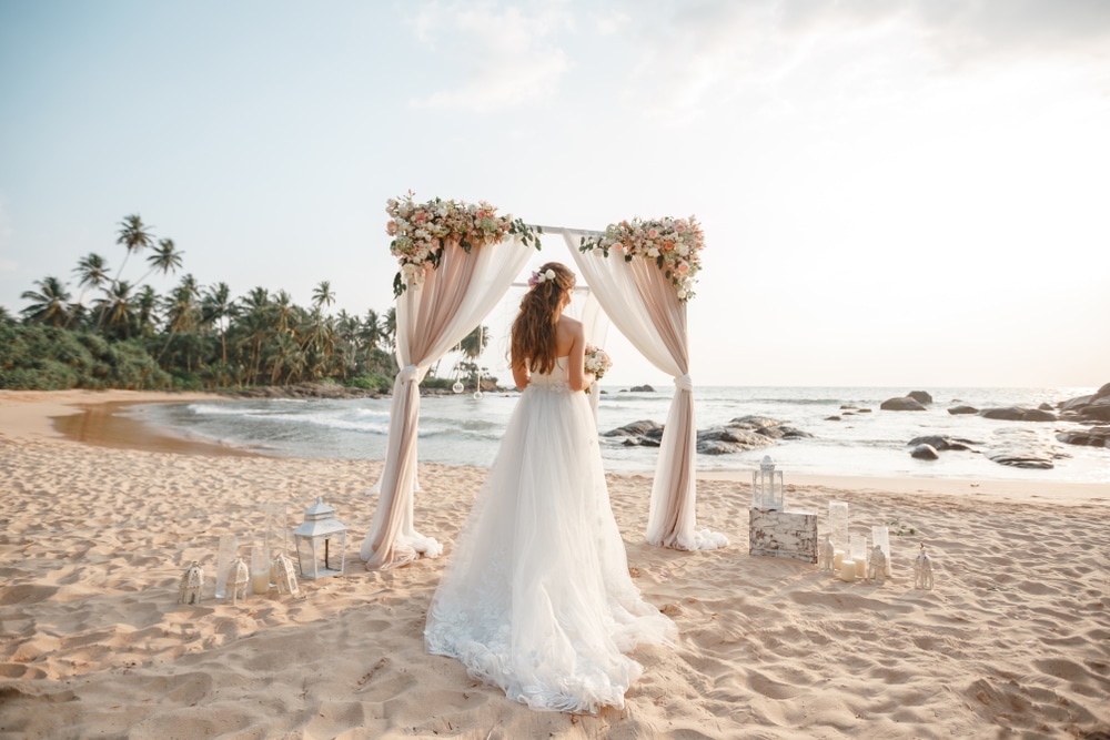 Portrait of stunning bride with long hair posing with great bouquet in front of the ocean under wedding arch