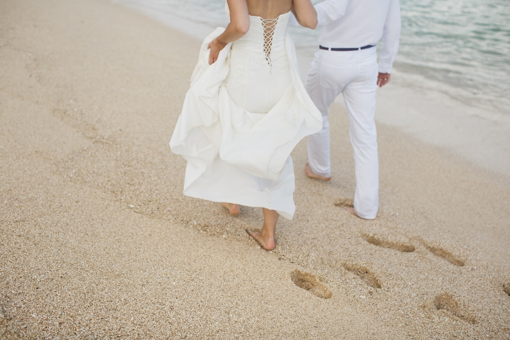 The Bride And Groom Walk Hand In The Sand Footprints