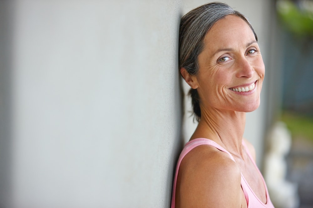 Portrait of an attractive mature woman in gymwear leaning against a gray wall.