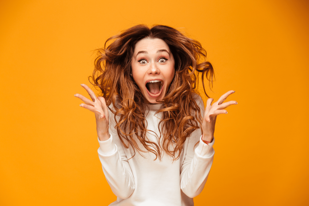 candid picture of excited screaming young woman standing isolated over yellow background.